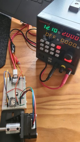 The XIAO RP2040 breadboard setup powered from a HANMATEK HM310T power supply showing 12.10 V and a 2.000 A limit, with the motor and coupling in the foreground.