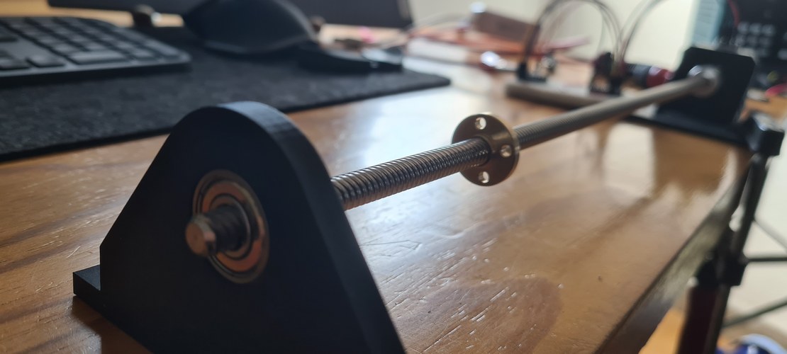 A T8x8 lead screw running through a printed bracket that holds a 608ZZ bearing at the free end, with the brass flanged nut on the thread, laid out on the desk.