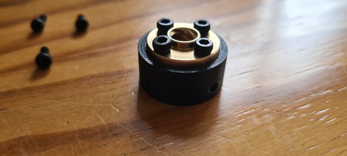 A black printed cylindrical nut block with a brass T8 flanged nut bolted into its top face by four black M3 socket-head screws.