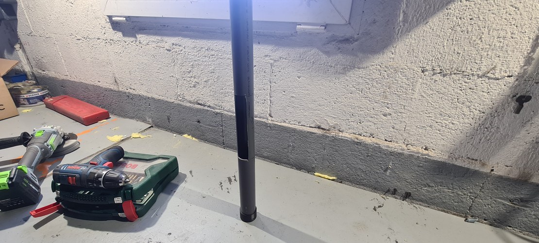 A grey PVC tube body standing vertically, prepared on the workshop floor with an angle grinder and a drill nearby.