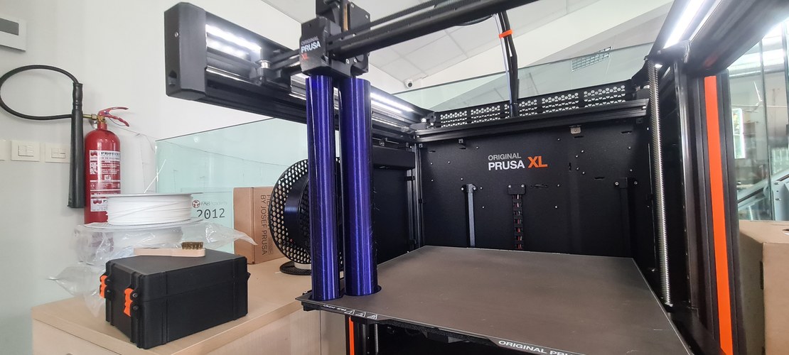 Side view of the Original Prusa XL mid-print, the tall blue PETG body rising off the bed.