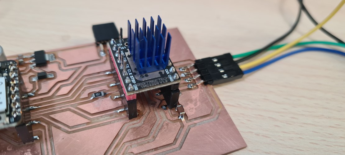 The TMC2209 stepper driver with blue heatsink seated in its staggered socket on the milled copper board, motor wires on a header to the right.