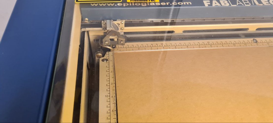 Cardboard sheet positioned against the ruler on the Epilog bed at Fab Lab León.