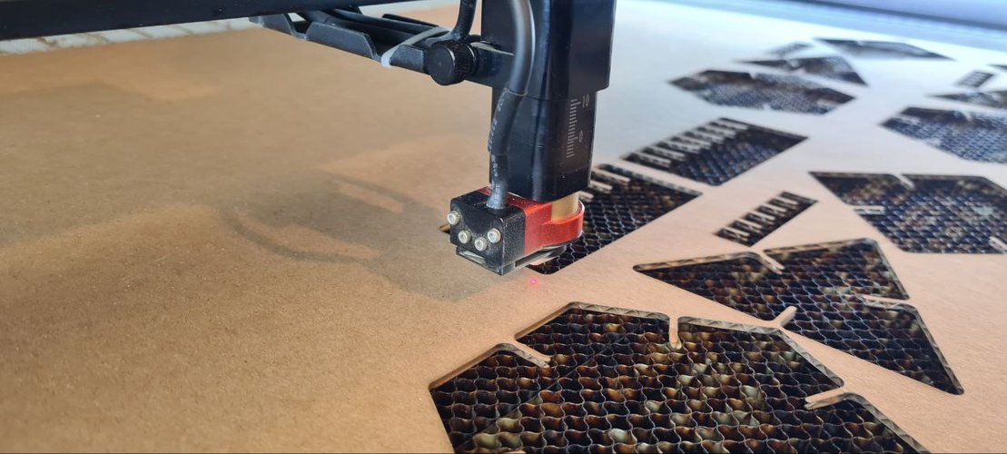 Close-up of the Framun laser head and freshly cut cardboard pieces on the honeycomb bed.