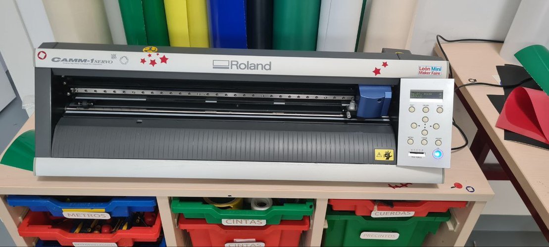 Roland GX-24 (CAMM-1 Servo) vinyl cutter on its cart at Fab Lab León, with rolls of vinyl stored behind it.