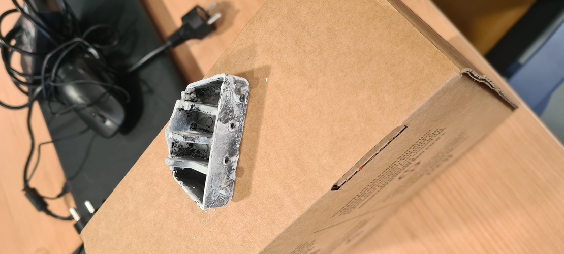 Small broken plastic part placed on a cardboard box for scanning.