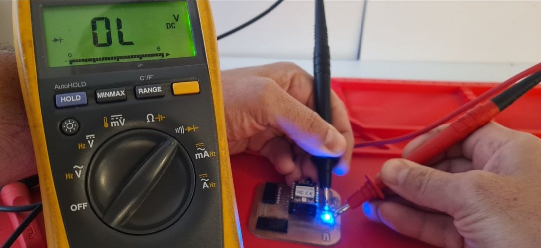 Fluke 179 in diode-check mode reading OL while the board's blue LED lights up under the probes.