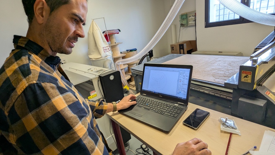 Working at the Dell laptop running VCarve Aspire next to the TEC-CAM 500, studying the toolpath setup with a previously cut martyr board visible on the machine table.