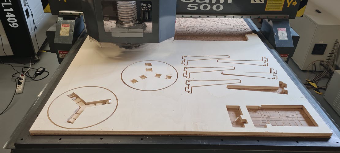 Wide view of the TEC-CAM 500 mid-cut on a shared production board with multiple simultaneous student projects visible: circles, leg sets, rectangular frames.