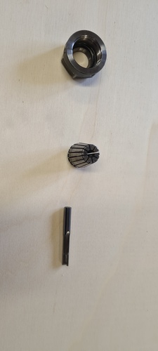 Three components of the collet system laid out vertically on a white surface: collet nut at top, ER collet in middle, 6 mm end mill at bottom.