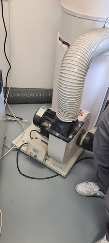 Small white portable dust extractor unit with motor and flexible white hose on the floor next to the CNC machine.