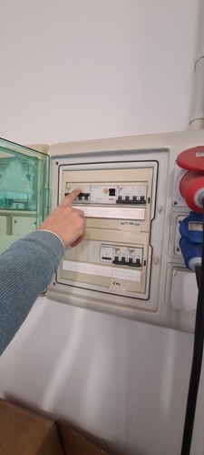 Open electrical panel showing differential switches with a hand pointing at the main breaker labeled for the CNC machine.