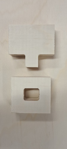 Two small plywood test pieces for the cross-slot joint, separated: one with a T-shaped tab and one with a rectangular slot with T-bone reliefs at the four interior corners.