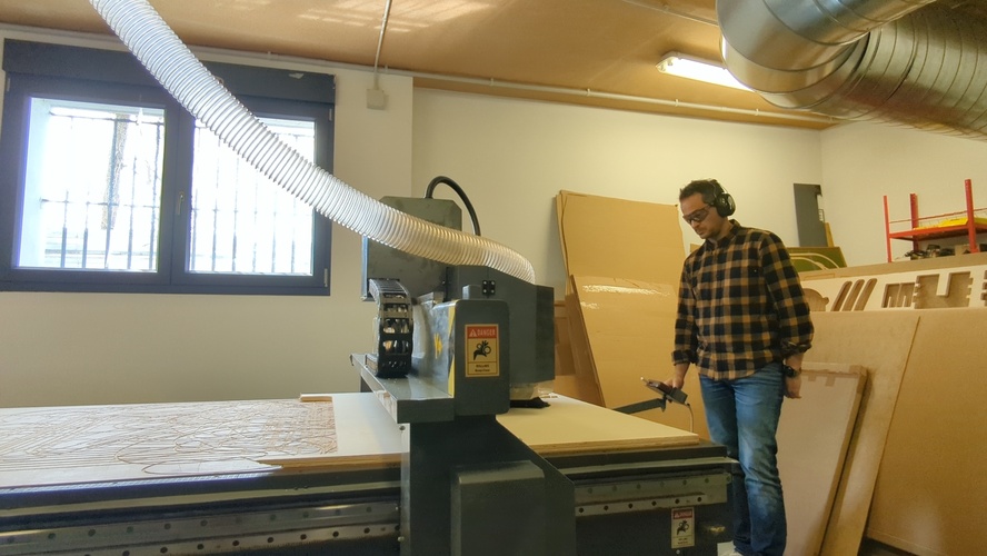 Standing at the side of the TEC-CAM 500 with the RichAuto controller in hand, overseeing a cut in progress with the board visible on the table.