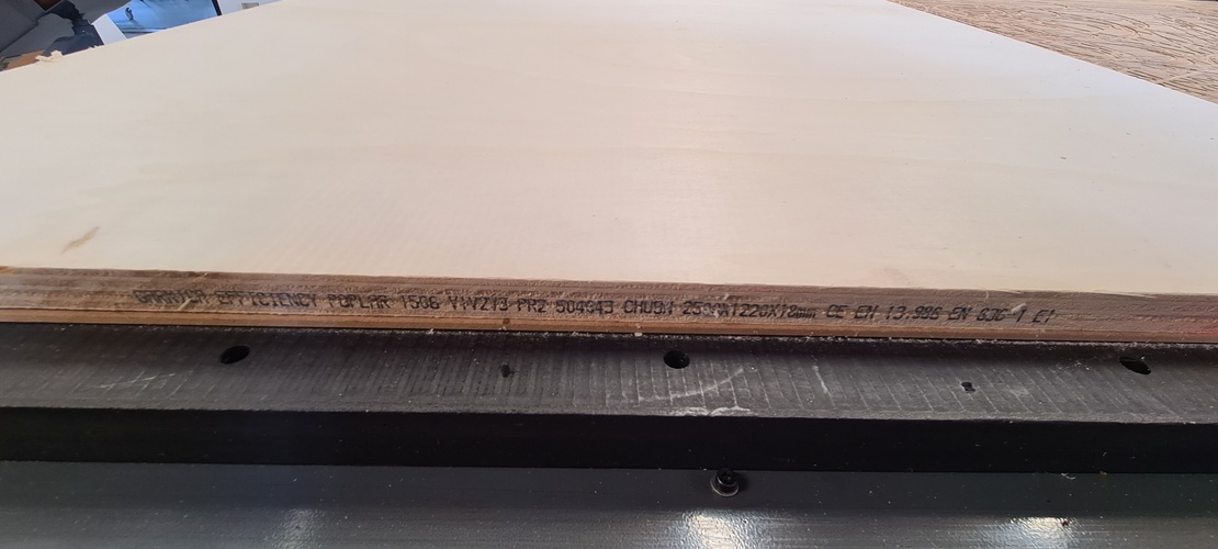 The edge of the plywood sheet showing the manufacturer's ink stamp with material grade, dimensions, and CE certification codes.