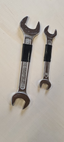 Two flat spanners — 27-30 mm and 18-21 mm — with black tape grip on the handles, lying on the machine table.