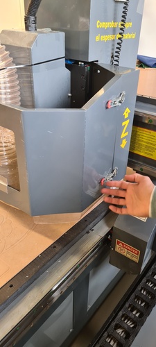 A hand opening the side access panel of the CNC spindle housing to reach the collet nut.