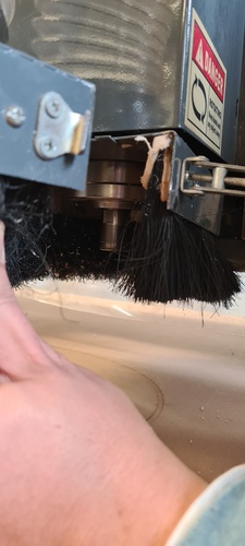 The CNC spindle head from below showing the installed end mill protruding below the dust collection brush skirt.