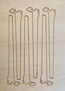 Six freshly cut plywood leg pieces laid out on the CNC table, each with a stepped joint profile at top and bottom.