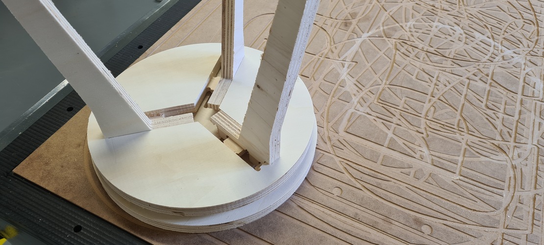 Close-up of the stool base inverted, showing the cross-slot joint where the two legs meet, with the pieces fitting but visibly strained and not fully at 90 degrees.