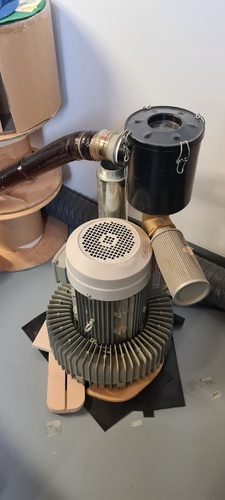 The vacuum pump motor with its filter and exhaust hose, sitting on the floor next to the machine.