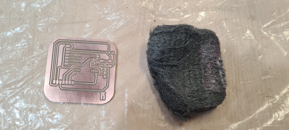 Milled PCB next to a pad of steel wool on a work surface, prior to cleaning.