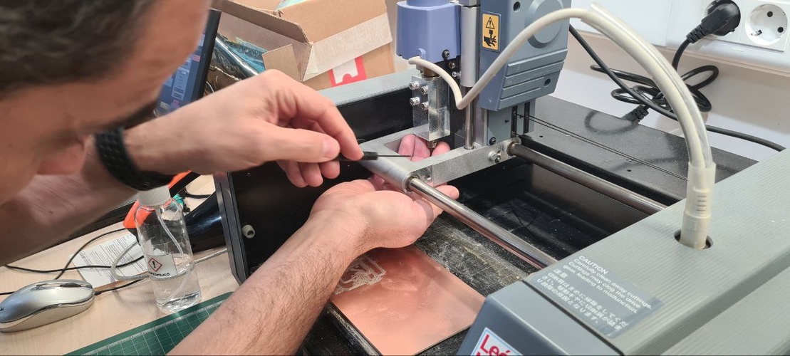 Hands inserting the 1/32 inch cutout end mill into the MDX-20 collet after the traces job, board with milled traces visible on the sacrificial surface below.