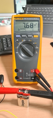 Fluke 179 True RMS multimeter showing 7.68 V DC reading, connected to a 9V Energizer battery with red and black crocodile clips.