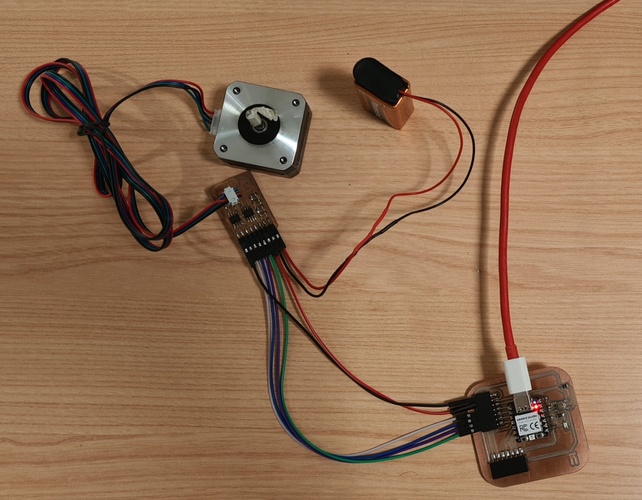 Complete test setup on a wooden table: NEMA 17 stepper motor connected via four-wire cable to Adrián's A4953 driver board, which connects via a ribbon cable to the XIAO RP2040 week 08 board. A 9V battery provides motor power via red and black wires. A USB cable connects the XIAO to the computer.