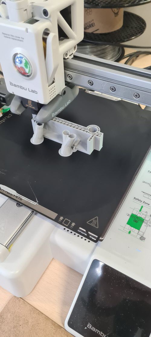 Bambu Lab A1 mid-print with grey PLA support pieces visible on the PEI plate and the toolhead laying the next layer.