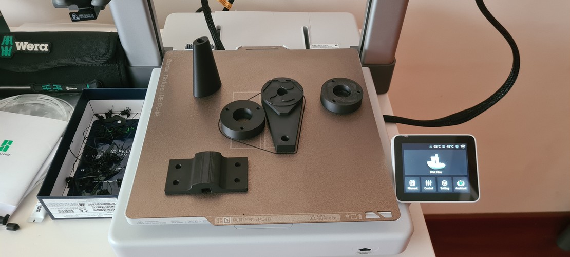 Close-up of a printed circular bracket in black PLA, showing some stringing inside the central hole.