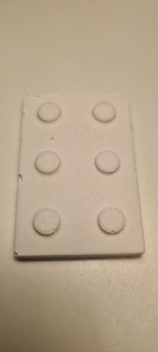 Plaster cast from the FDM-printed PLA master (Track B): a white 2x3 brick face with a clean, smooth surface and six well-formed studs, shallower in relief, with no visible lines.