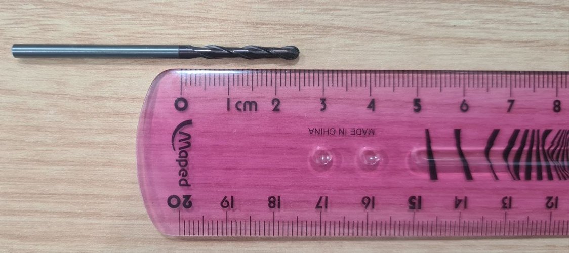 Close-up of the tapered ball-nose endmill next to a centimetre ruler, showing the cone shape opening from the tip towards the shank