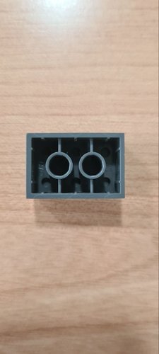 Underside of a real grey LEGO 2×3 brick on a wooden bench, showing the hollow interior, two central tubes and the side ribs