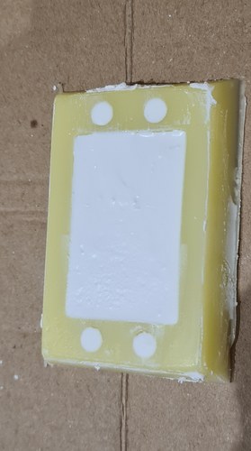 White Michelangelo plaster poured into the yellow silicone mould, filling the central brick cavity and the four corner stud holes, setting on a cardboard surface.