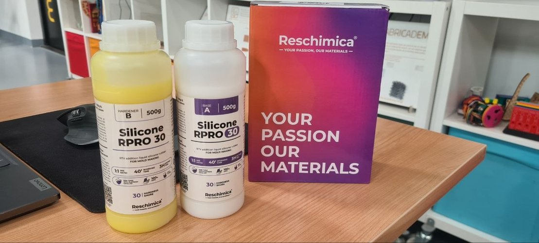 Two 500 g bottles of Reschimica RPRO 30 silicone (Base A and Hardener B) next to the manufacturer's box on a wooden bench at Fab Lab León