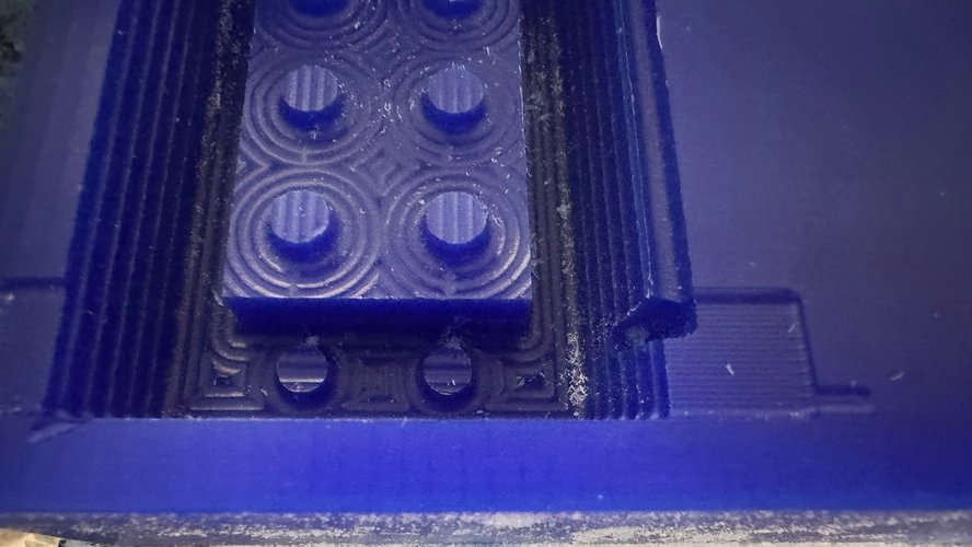 Macro photo of the brick top after the rough pass. The studs are still cylindrical, and the wax around each stud and around the brick contour shows concentric step-down rings — the trace of the 3 mm flat endmill descending in 3 mm layers, each layer following the contour at a slightly lower Z.