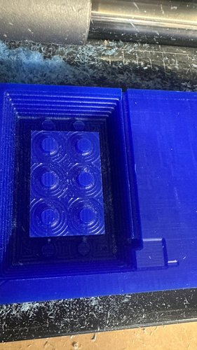 Top-down view of the wax stock after the rough pass: the brick contour is recognisable in the centre, surrounded by the rectangular foso cleared by the rough. The six studs appear as smooth cylinders standing on top of the brick body, not yet detailed.
