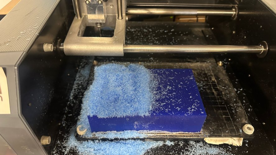 Roland MDX-20 work area mid-job: the 3 mm flat endmill is descending into the Ferris File-A-Wax Blue stock during the rough pass, with a thick pile of blue wax chips covering the left half of the block.