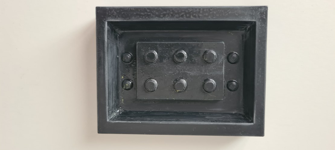 Top-down view of the wet-sanded, dried master sitting in its integrated casting box. The brick face is matte with light sanding marks; the studs and the corner witness studs are intact.
