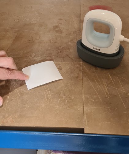 The small Cricut heat press on its base on the workbench, patch ready beside it.