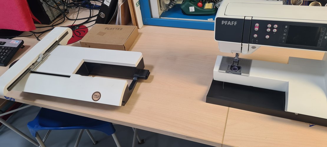 Wide bench shot with the embroidery arm on the left and the PFAFF machine on the right, separated.