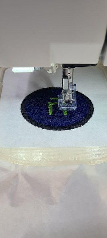 Close-up with the dark satin border now stitched around the blue circle, framing the design.