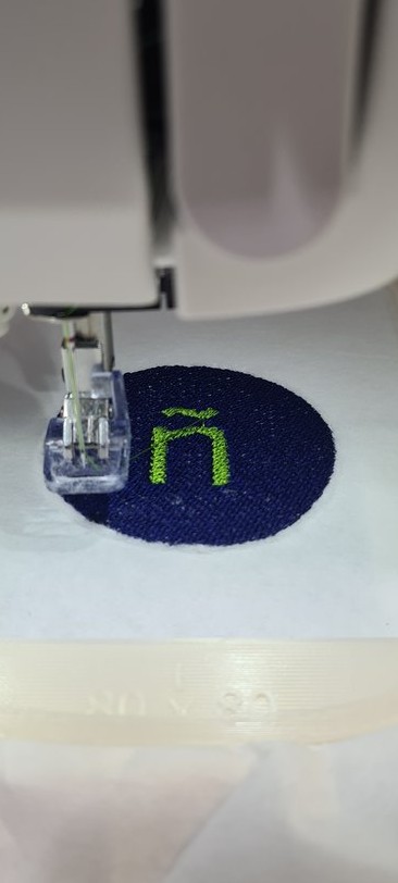 Close-up: the blue fill done with the lime-green ñ stitched on top, no dark border yet.