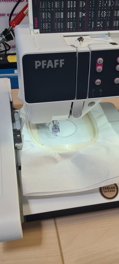 The machine starting: only a thin dashed outline circle stitched on the white stabiliser, no fill yet.