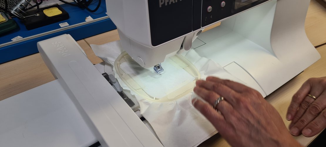 The 80x80 hoop with stabiliser mounted on the embroidery arm under the needle, hands holding it.