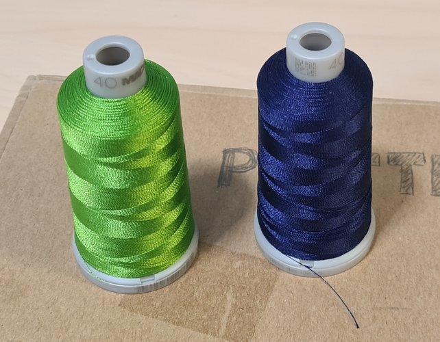 Two embroidery thread spools side by side, lime green and navy blue.