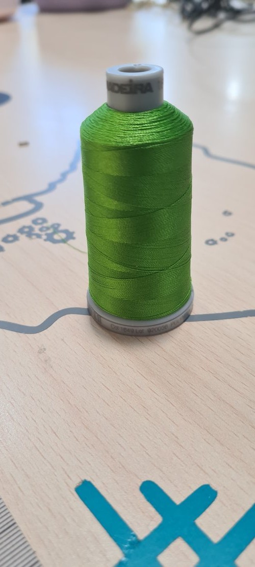 A single lime-green embroidery thread spool standing on the bench over the project plan.