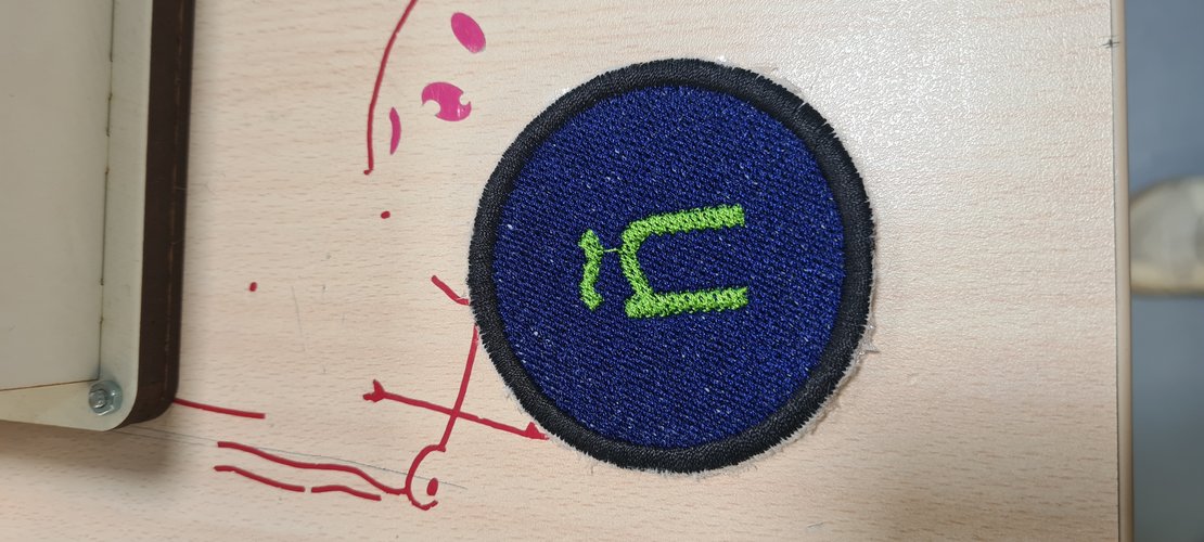 The finished, trimmed ñ patch on the workbench: blue fill, lime-green ñ, dark satin border.