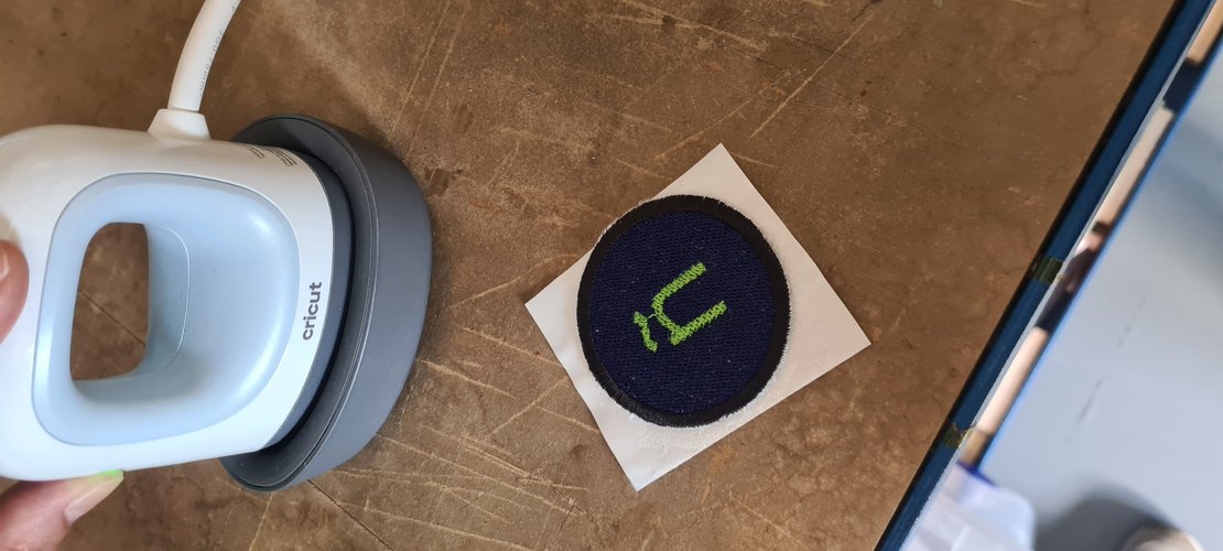 The patch face-up on the adhesive paper next to the Cricut press, ready to be heat-set.